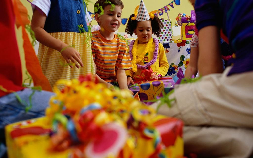 A group of children with birthday hats, leis, gifts and streamers at a party. 