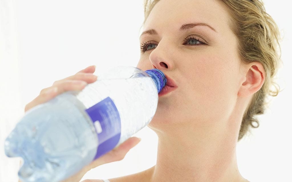 A young woman drinking water out of a plastic bottle.