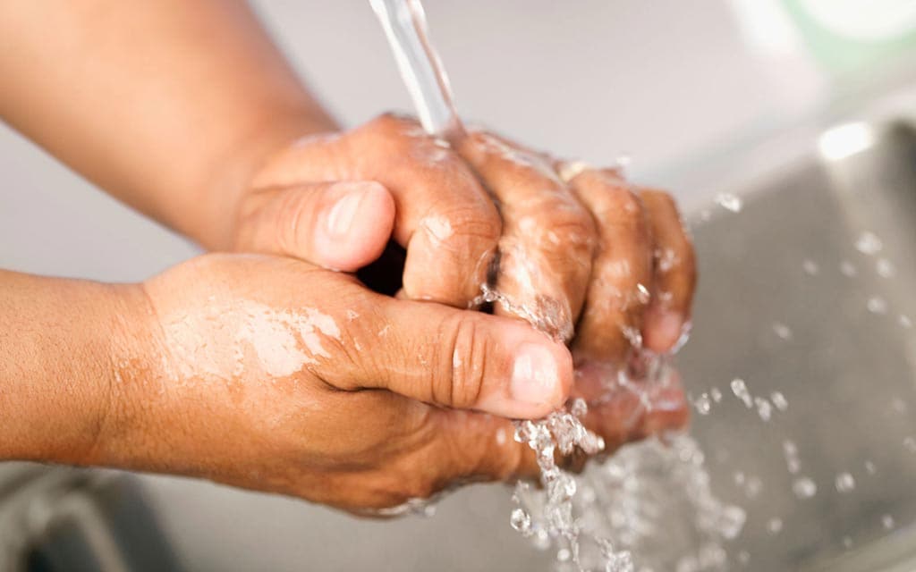 A person washing hands under running water.