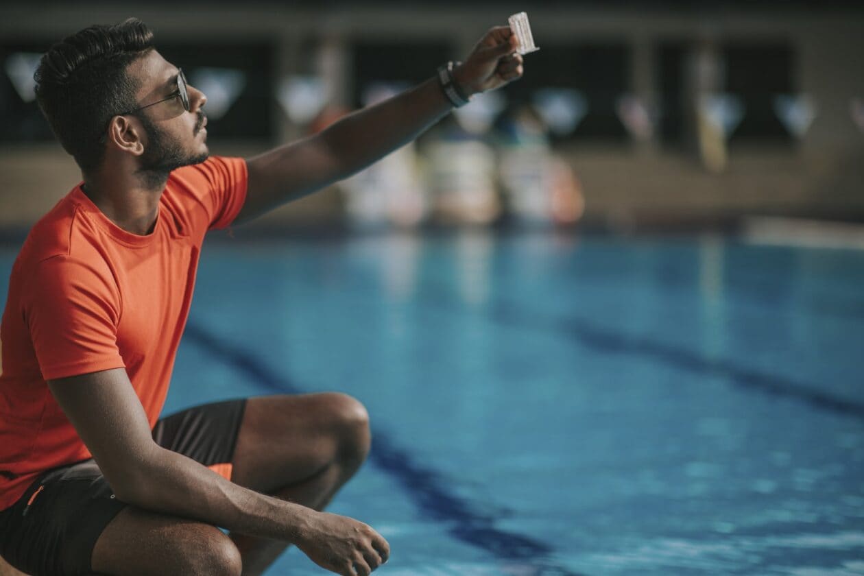 A male lifeguard tests the water at an outdoor pool.