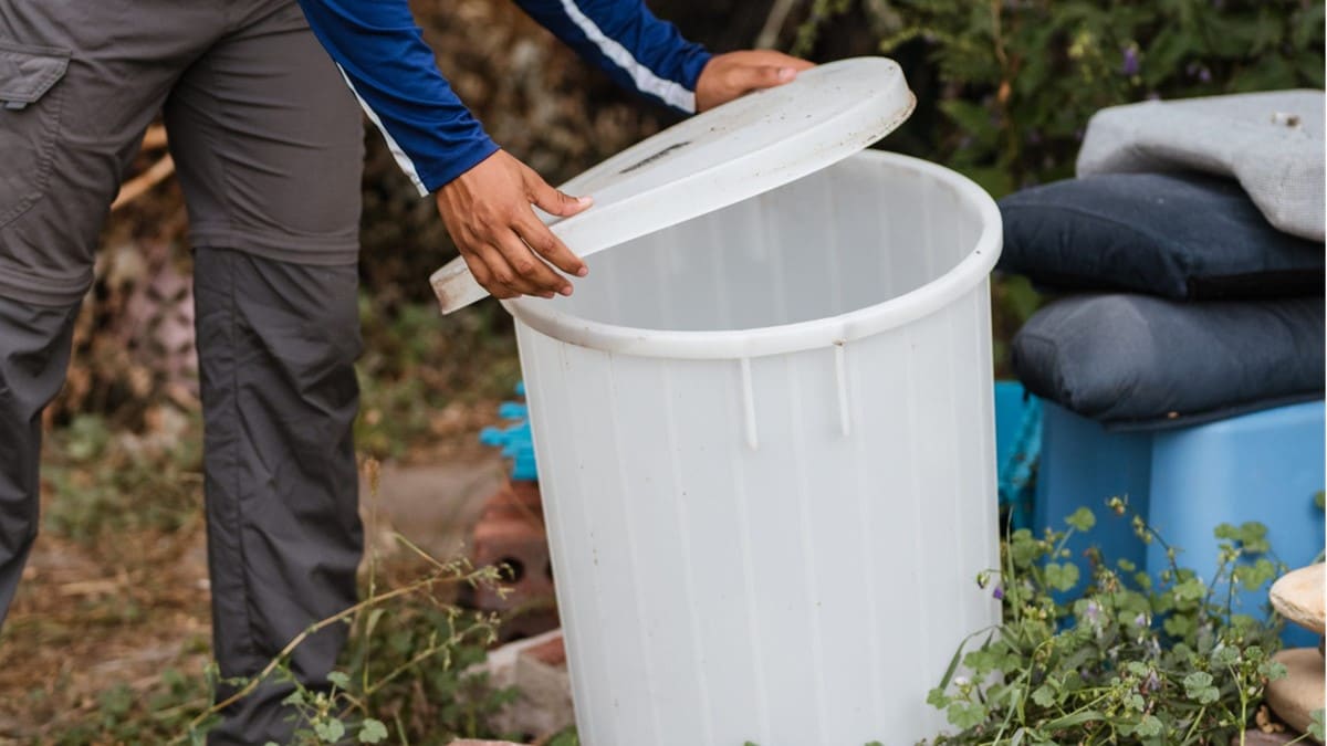 Person covering a bucket to keep mosquitoes from laying eggs in standing water.