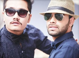 Two men wearing sun glasses and button up shirts, looking at something in the distance