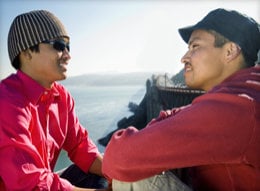 Two men sitting and talking with ocean in the background.