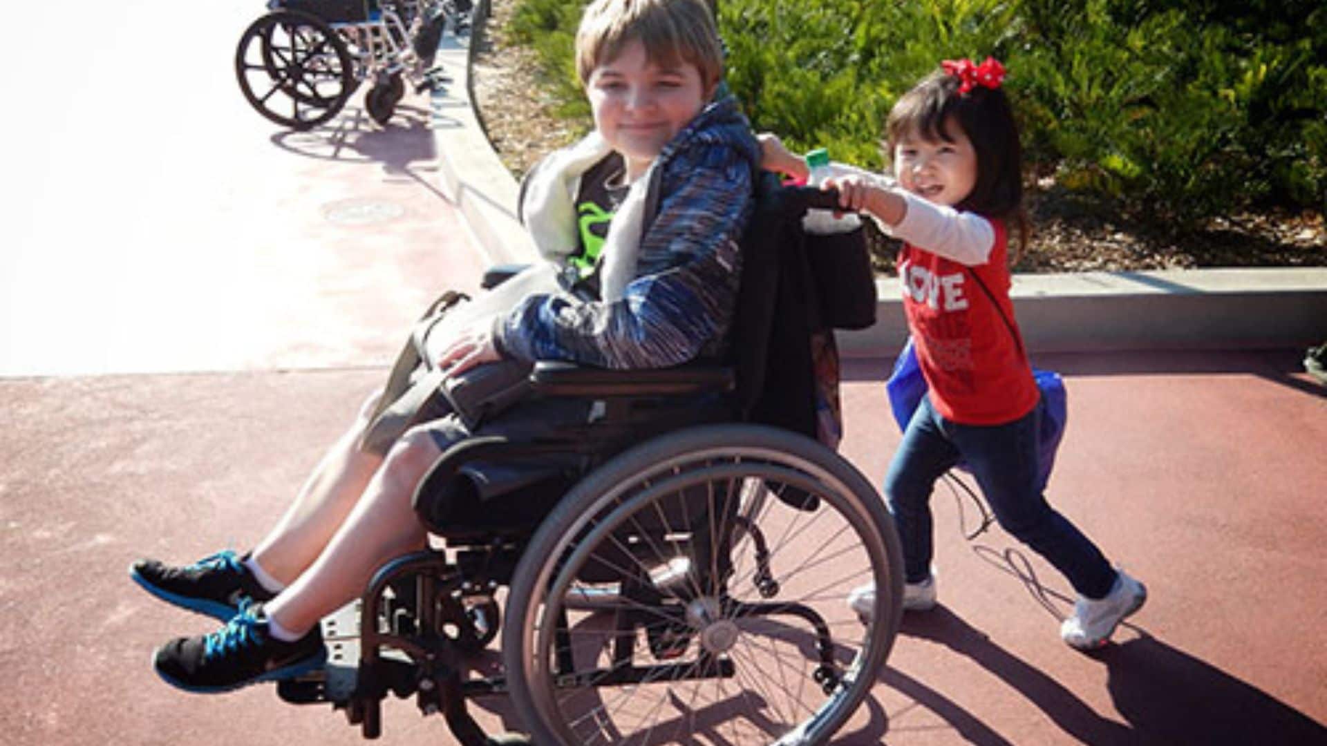 Small girl pushing boy in wheelchair