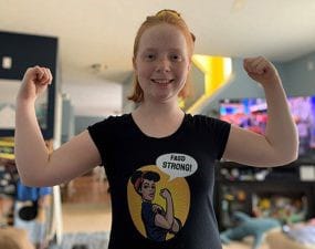 Brenna as a teen wearing a “We Can Do It!” parody shirt that says “FASD Strong!” 