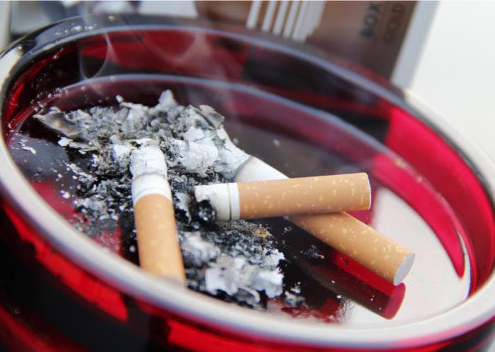 A bright red ashtray filled with smoldering cigarettes and ashes.