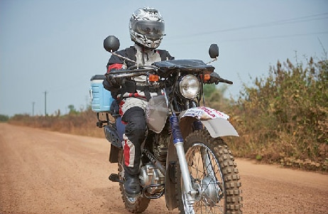 A motorcycle courier riding with ebola samples on a dirt road.