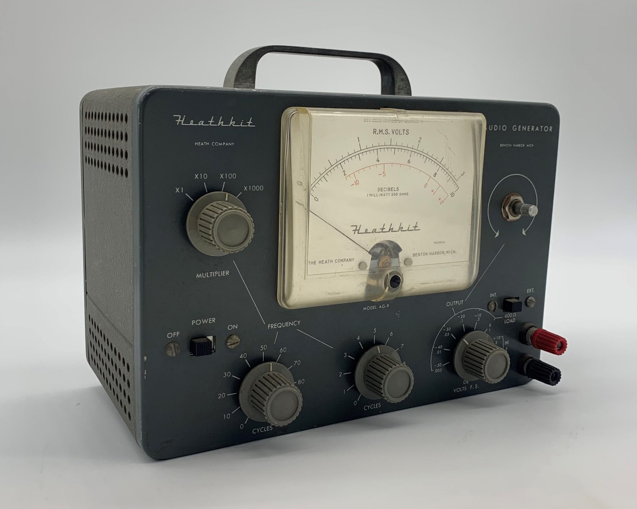 Heathkit Audio Generator consists of a dark gray box and a frequency monitor with indicator needle. The kit has knobs to adjust the audio input’s multipliers, cycles, frequency, and voltage.