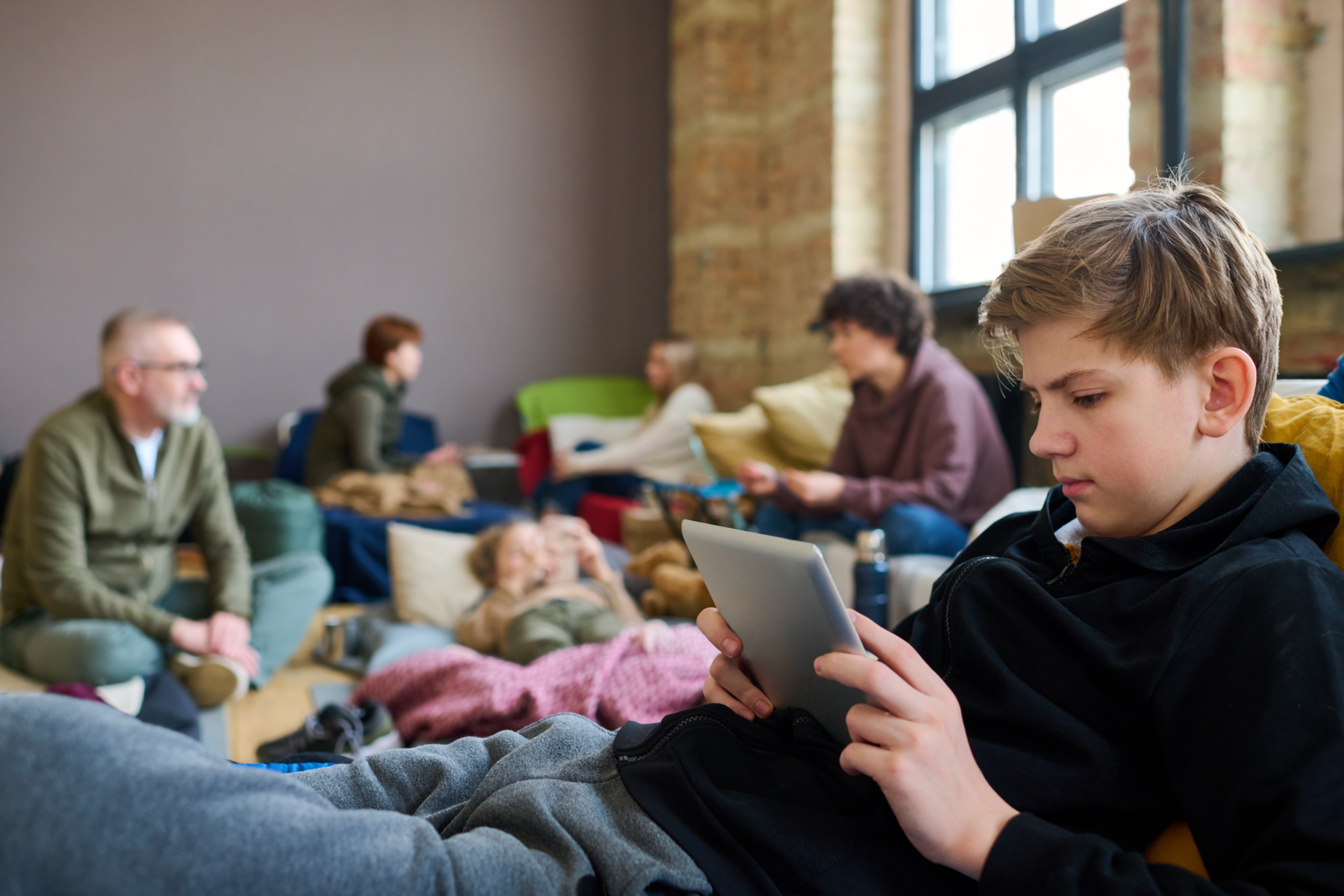 Teen boy using a tablet while sitting in a disaster shelter.