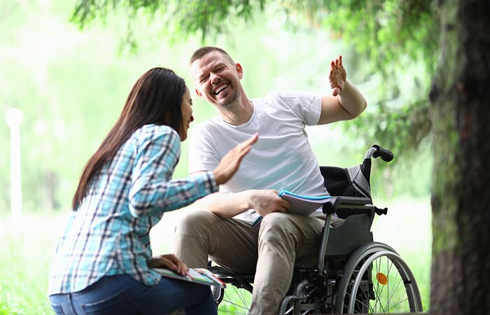 Happy friends hanging out in the park, a young woman and a man in a wheel chair