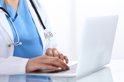 Doctor typing on laptop computer Doctor typing on laptop computer while sitting at the glass desk in hospital office