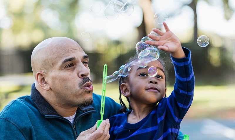 2021 Community Report cover - Little boy watching father blow bubbles with wand