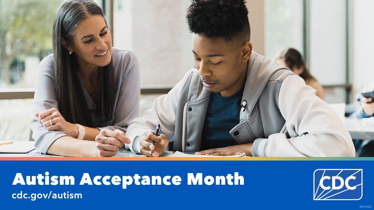 A teacher sits with a high school student who is writing in a notebook during class. Text overlay reads, “Autism Acceptance Month. cdc dot gov slash autism”