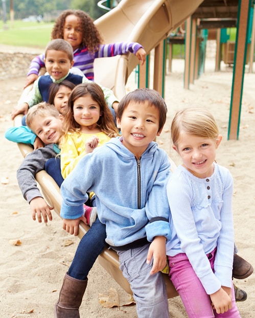 Diverse smiling kids together on a slide at a playground