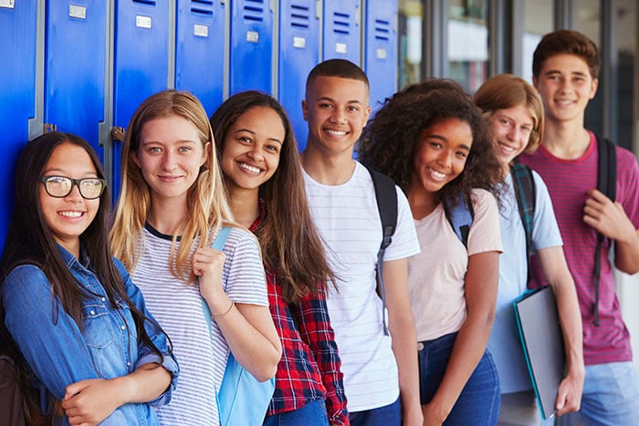 Teenage school kids smiling to camera in school hallway