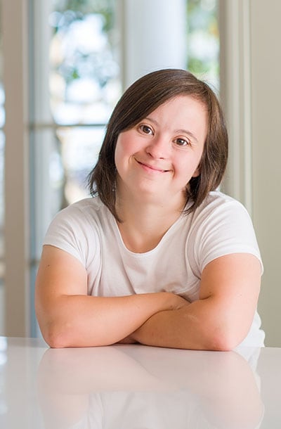Down syndrome woman at home with a happy face smiling with crossed arms