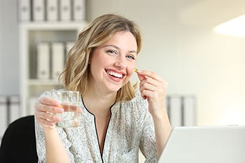 Happy office worker showing a vitamin supplement pill