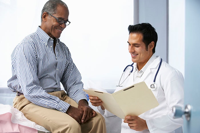 Doctor In With Male Patient Reading Notes