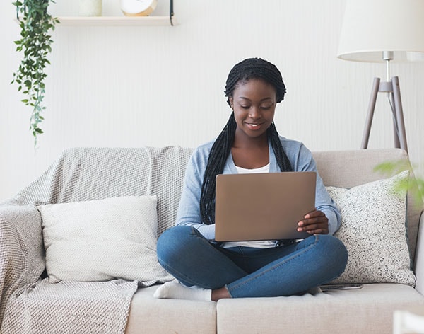 Black woman working with laptop computer on sofa