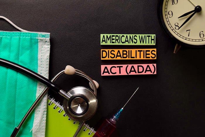 Americans with Disabilities Act written on a dark desk with a stethoscope, mask, and other health care provider items.