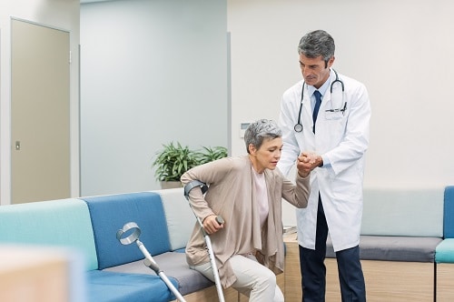 Male doctor helping elderly female patient stand up