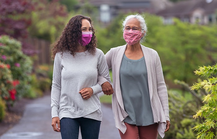 Mujer mayor y su hija adulta disfrutando juntas al aire libre, usando mascarillas protectoras