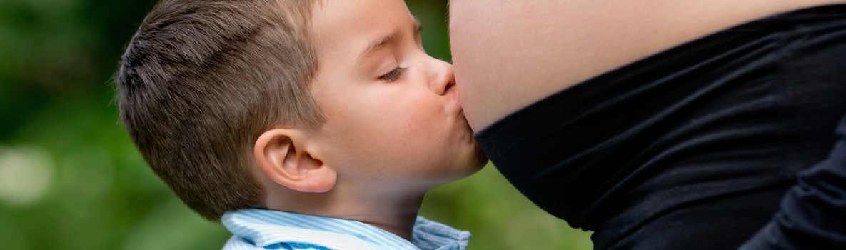Niño pequeño besando el vientre de su madre embarazada.