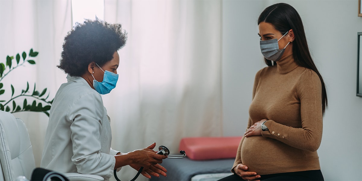 Young pregnant woman on a visit to doctor. Wearing protective masks during corona virus epidemic