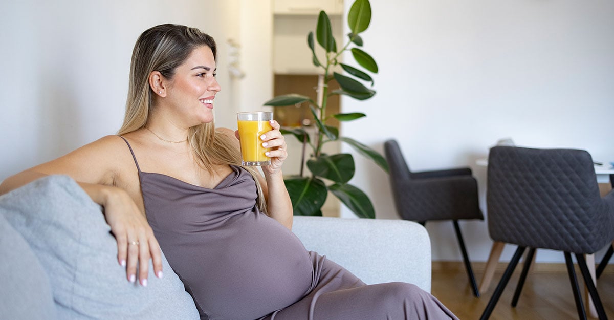 Pregnant woman sitting on couch with glass of juice