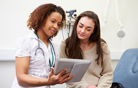 Health care worker looking at tablet with teenage girl