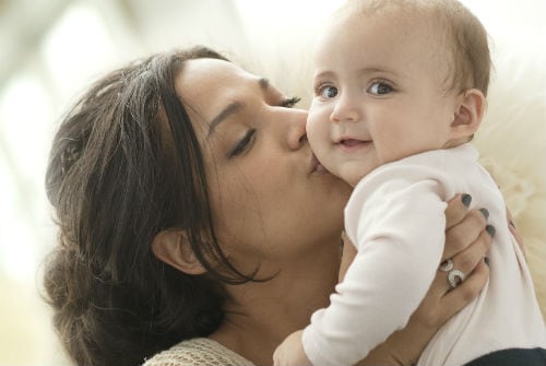 Photo of woman holding her baby and kissing cheek