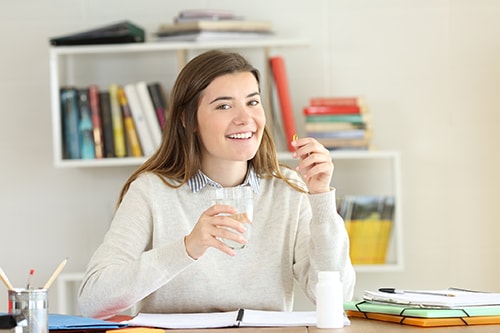 Happy student holding a vitamin pill on a desk