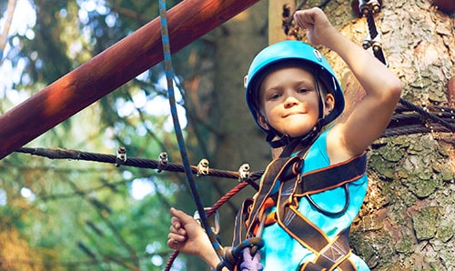 Little boy in a protective helmet and in special equipment passes an obstacle course at height
