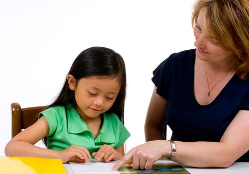 A young child sitting at a desk with her teacher