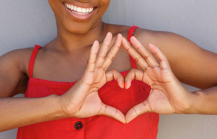Woman making a heart sign with fingers over her heart and smiling