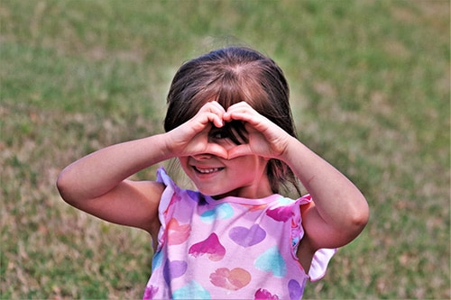 Little girl making a heart gesture with her hands up to her face