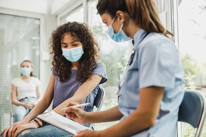 A masked young woman and her healthcare provider having a conversation in a waiting room