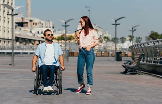 A man in a wheelchair chatting outside with a girl friend.