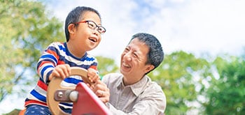 A small child with down syndrome is enjoying with his father at a public park on a sunny day.