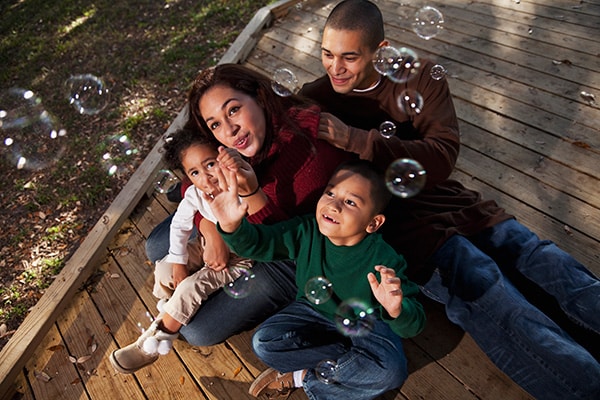 Family sits on a deck together looking up at bubbles