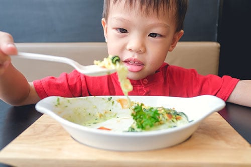 A young boy eating a plate of vegetables