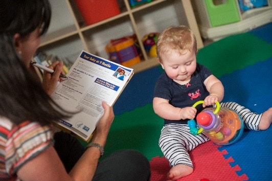 A child playing with toys while care provider tracks milestones
