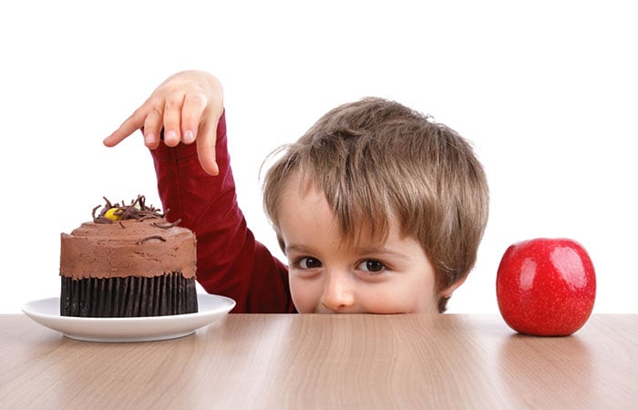 Child at a table choosing between cake or an apple