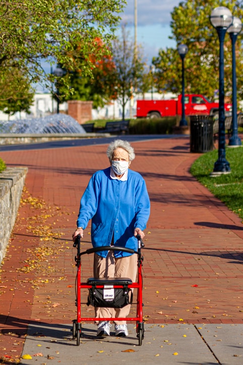 A senior woman is strolling in a park using her walker.