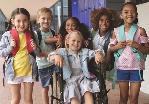 Happy school kids standing in corridor while schoolgirl sitting on wheelchair