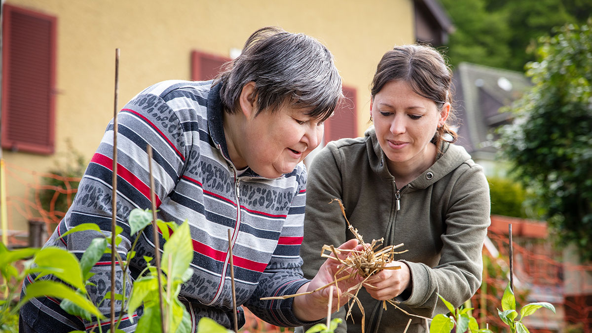 A caregiver helps a woman with a disability in the community garden.