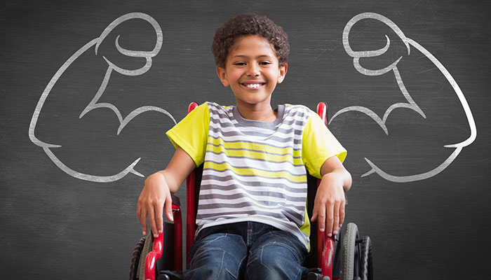 A boy in a wheelchair in front of flexing arms drawn on a chalkboard.