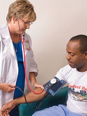 Female clinician in the process of conducting a blood pressure examination, upon a seated male patient in a clinical setting.