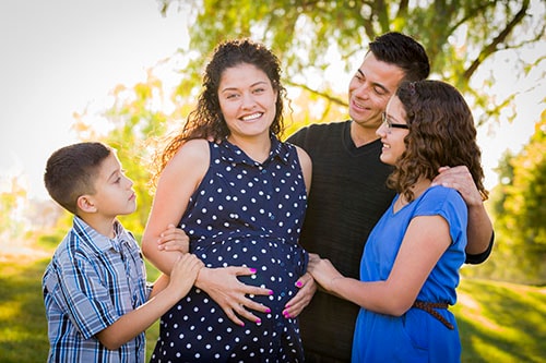 Familia hispana feliz con su madre embarazada al aire libre