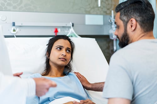 Una paciente en una cama de hospital mira con tristeza a un hombre que la consuela